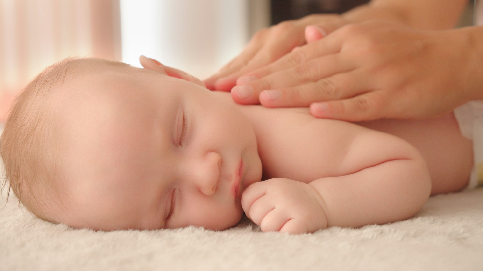 Mother doing massage on her healthy sleeping infant baby.